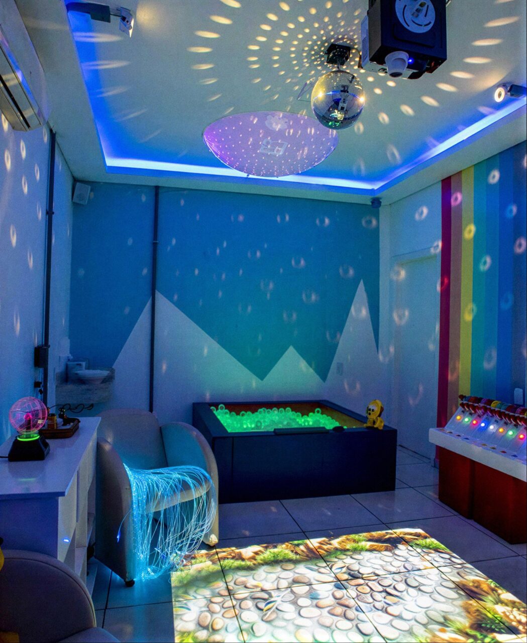 Sala multissensorial com luzes coloridas, piscina de bolinhas e piso interativo