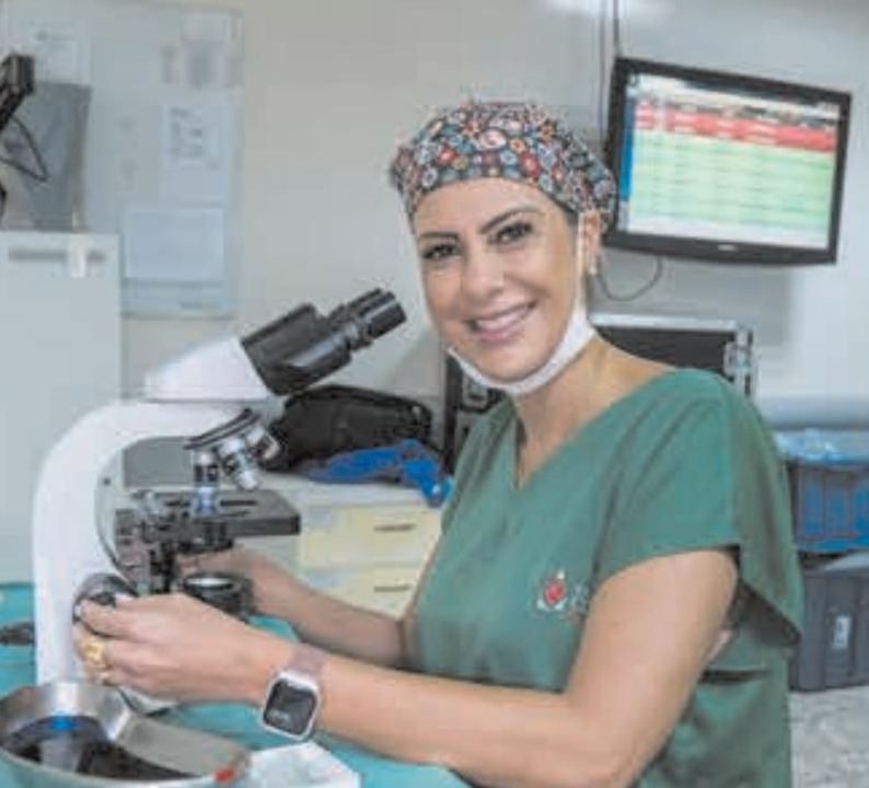 Profissional sorri ao lado de um microscópio no laboratório do CDM
