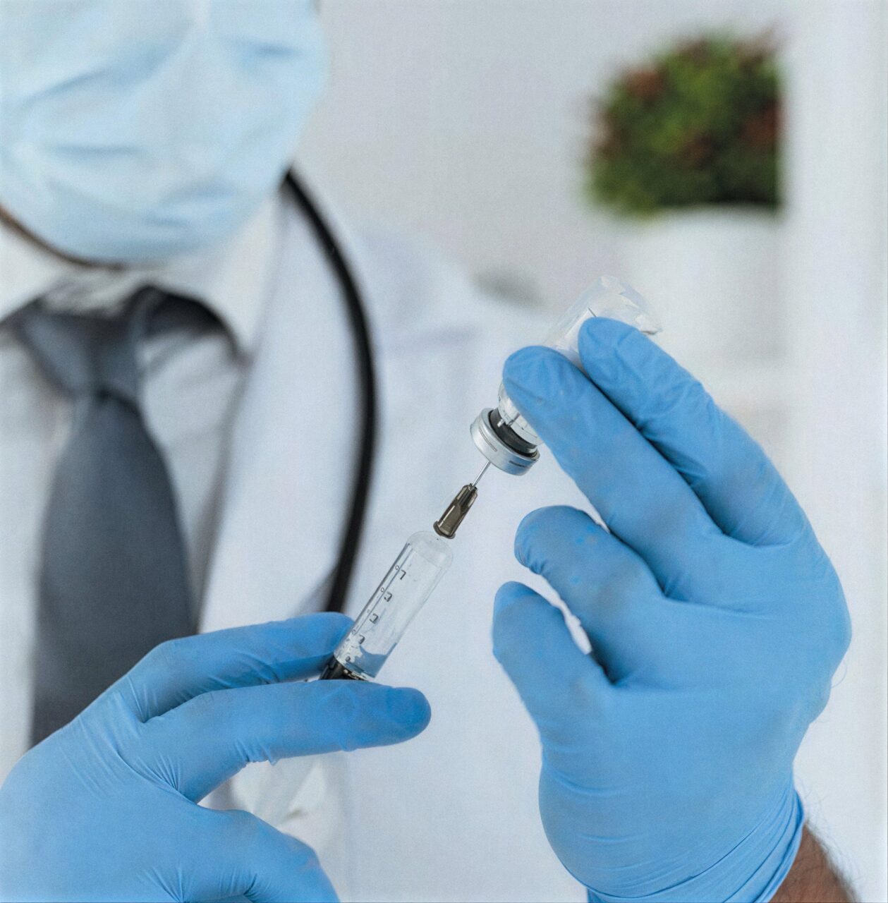 Mãos de luvas azuis preparando uma seringa de vacina